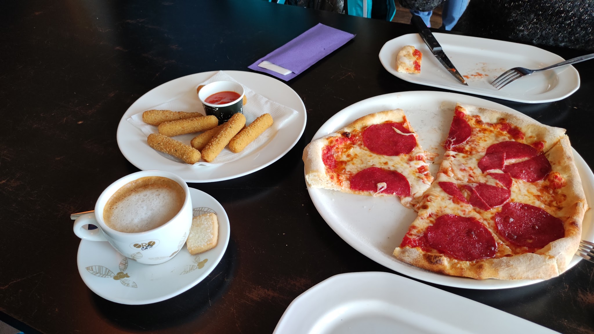 Pizza salami, mozzarella sticks met dip en een cappuccino op tafel