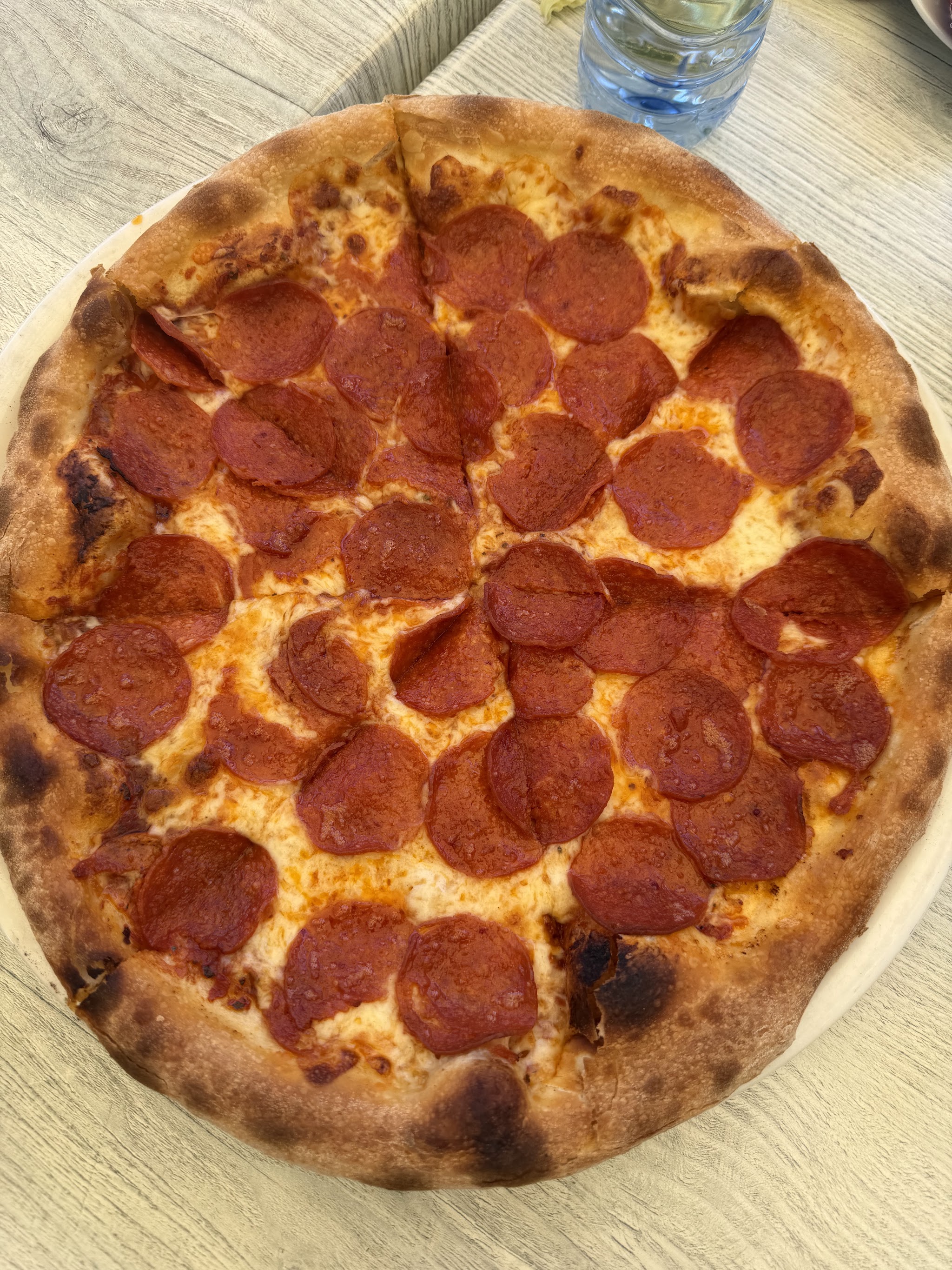 Een hele pizza salami met een gebleste rand op een houten tafel